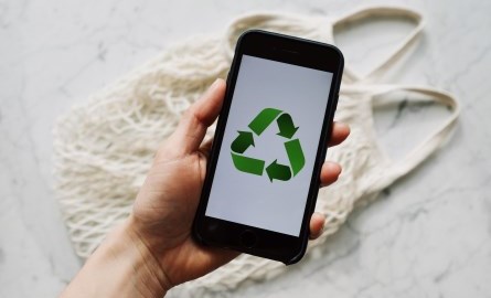 Hand holding smartphone showing recycle symbol